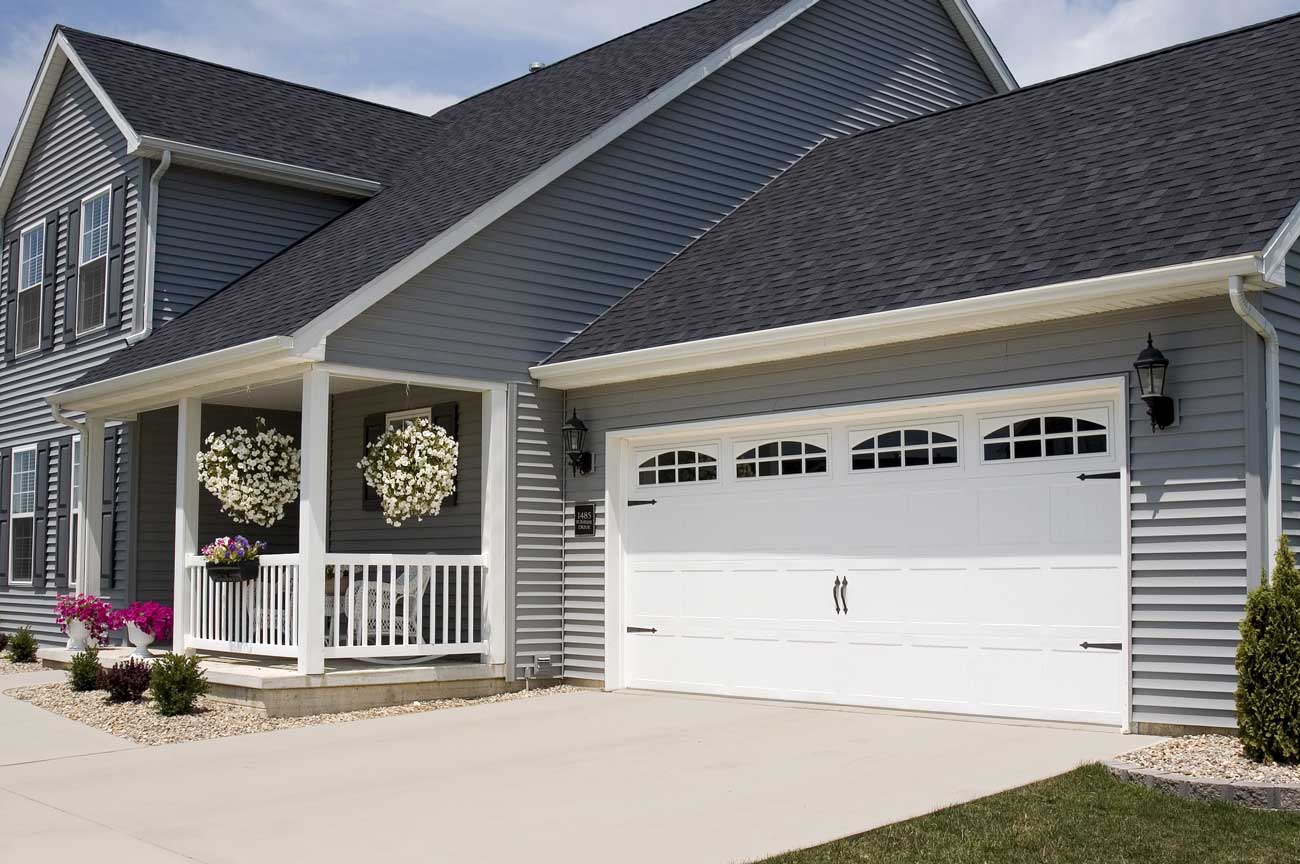 This is an image of white steel short panel garage doors with windows on a blue home.